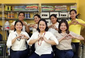 Happy Helpers founder Maan Sicam, centre, and colleagues smile and create a heart shape with their hands