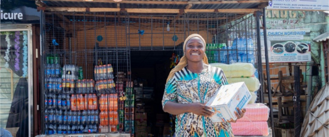 An African women smiles outside a shop, holding stock, courtesy of Omnibiz