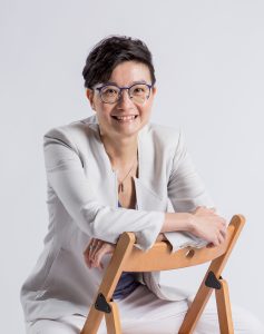 Winnie Mak sits in chair in white suit and smiles